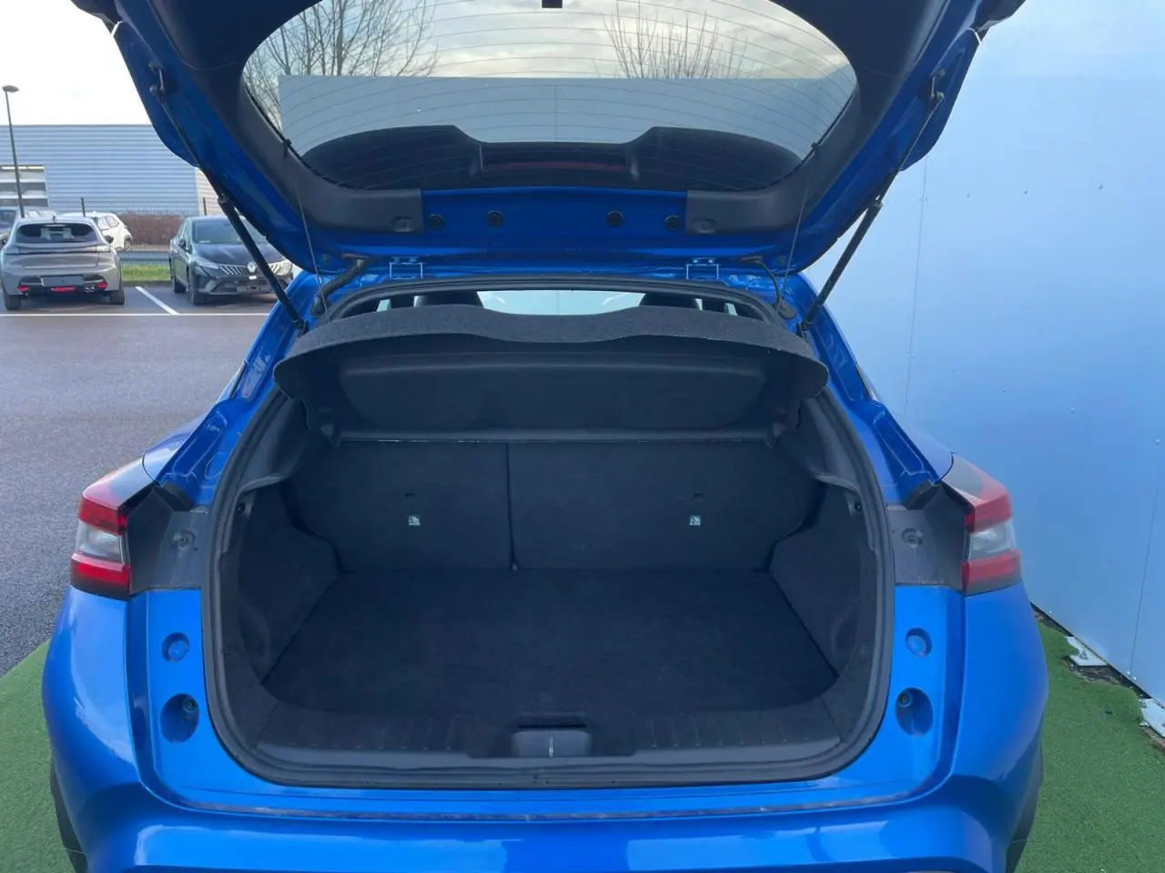 Coffre ouvert d'un Nissan Juke II 2024 bleu magnetic, vue arrière montrant l'espace de chargement vide.