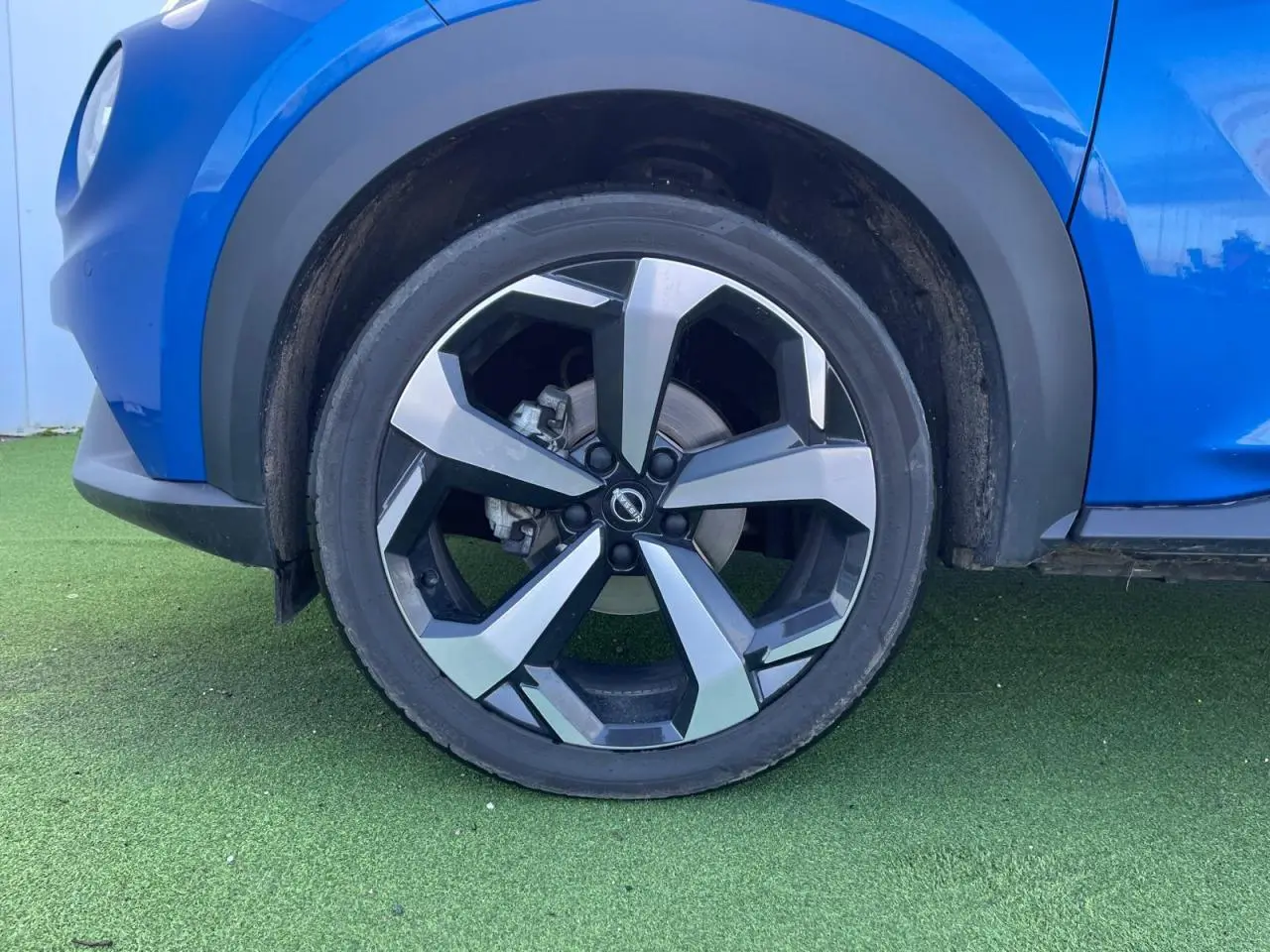 Gros plan sur la roue avant gauche du Nissan Juke II bleu magnetic avec jante alliage noire et argentée.