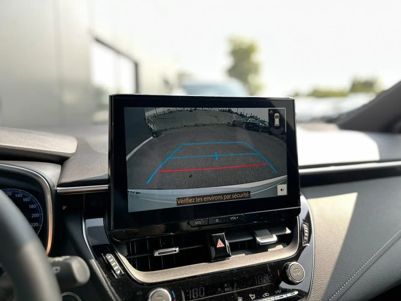 Écran central montrant la caméra de recul d'une Toyota Corolla Touring Sport blanche, vue intérieure avant.