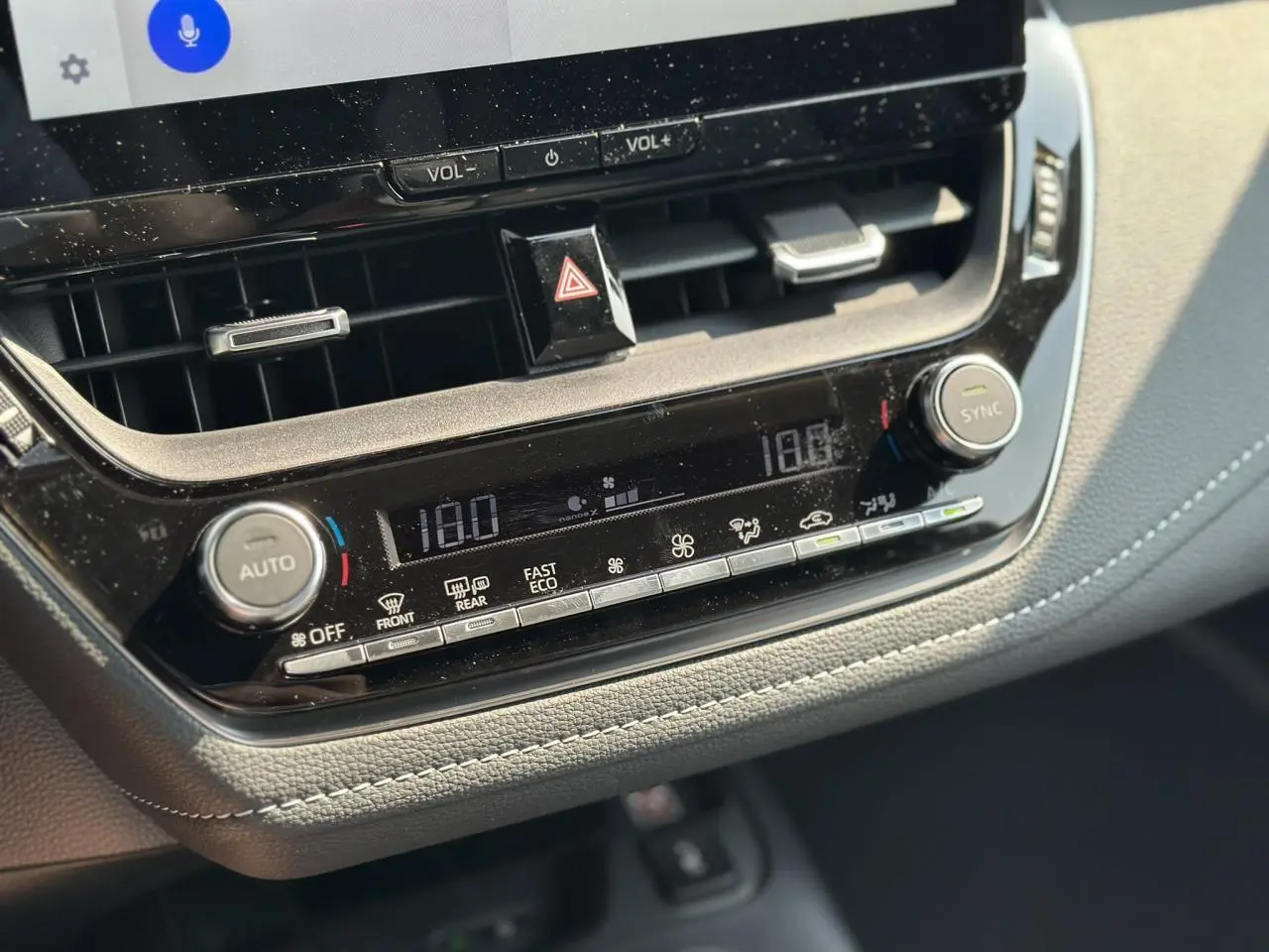 Gros plan sur la console centrale de la Toyota Corolla Touring Sport blanche, affichant la climatisation automatique bi-zone.