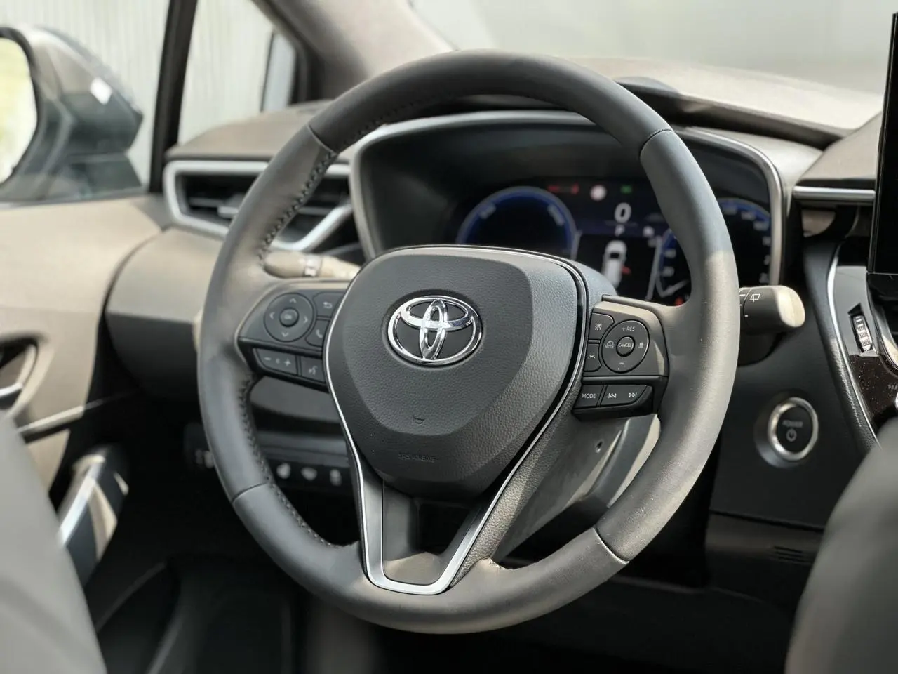 Volant multifonction noir de Toyota Corolla Touring Sport 2025, avec tableau de bord numérique et bouton démarrage visible.