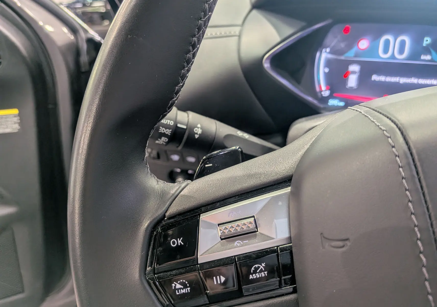 Gros plan sur le volant cuir noir du DS3 2024 gris Platinium, avec commandes intégrées et tableau de bord numérique en arrière-plan.