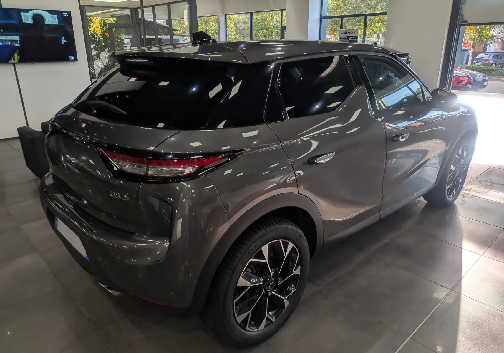 Vue 3/4 arrière droite d'une DS3 2024 Gris Platinium avec toit noir et jantes bi-ton en concession.