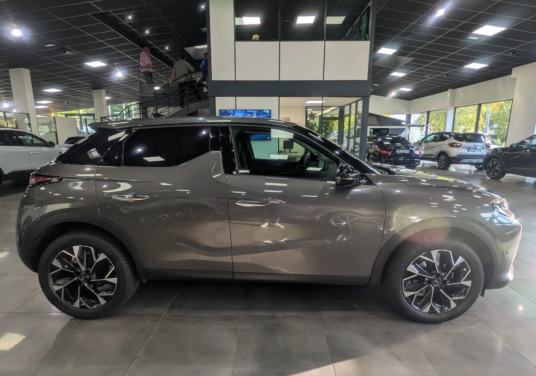 Vue de profil côté gauche du DS3 2024 gris Platinium avec toit noir et jantes bi-ton en concession.
