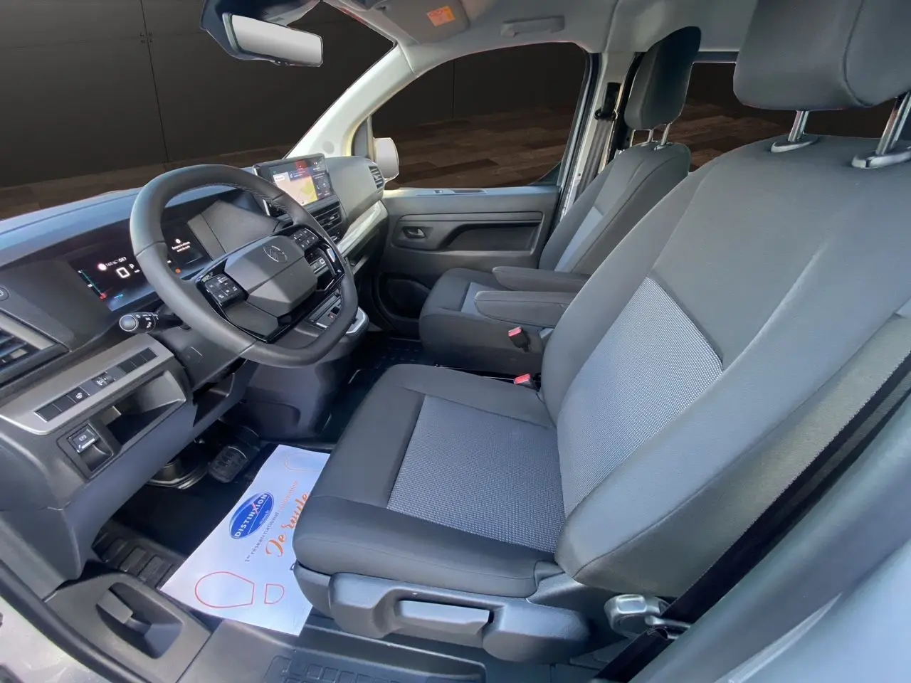 Intérieur avant du Citroën Jumpy XL gris acier, sièges tissu bi-ton noir-gris avec accoudoirs et tableau de bord moderne.