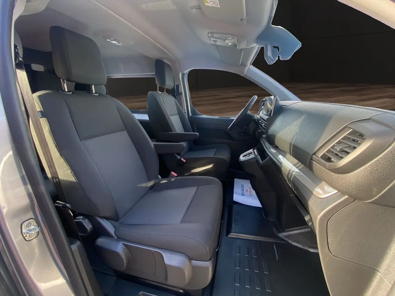 Intérieur avant du Citroën Jumpy XL gris acier, sièges tissu noir avec accoudoirs et tableau de bord moderne.