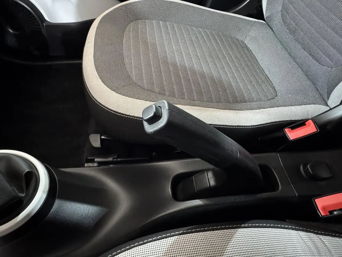 Vue rapprochée de la console centrale et frein à main entre les sièges gris clair et foncé d'une Renault Twingo blanche.