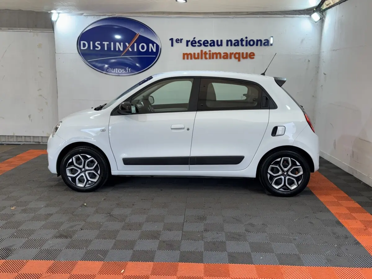Profil droit d'une Renault Twingo Equilibre blanche 2022, avec jantes distinctives et rétroviseurs noirs dans un showroom.