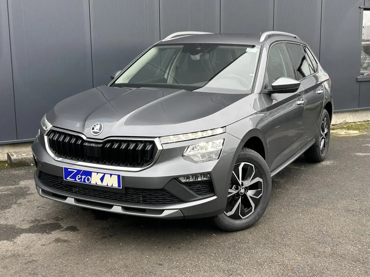 SKODA KAMIQ gris graphite en 3/4 avant droit, avec jantes alliage noires et baguettes chromées visibles.