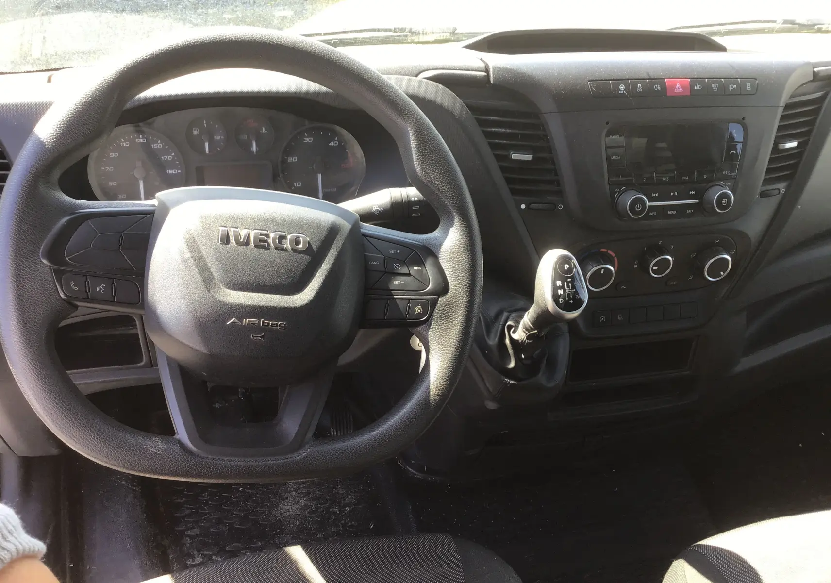 Vue intérieure centrée sur le volant noir IVECO et la console centrale avec levier de vitesses automatique du Daily Chassis Cabine blanc.