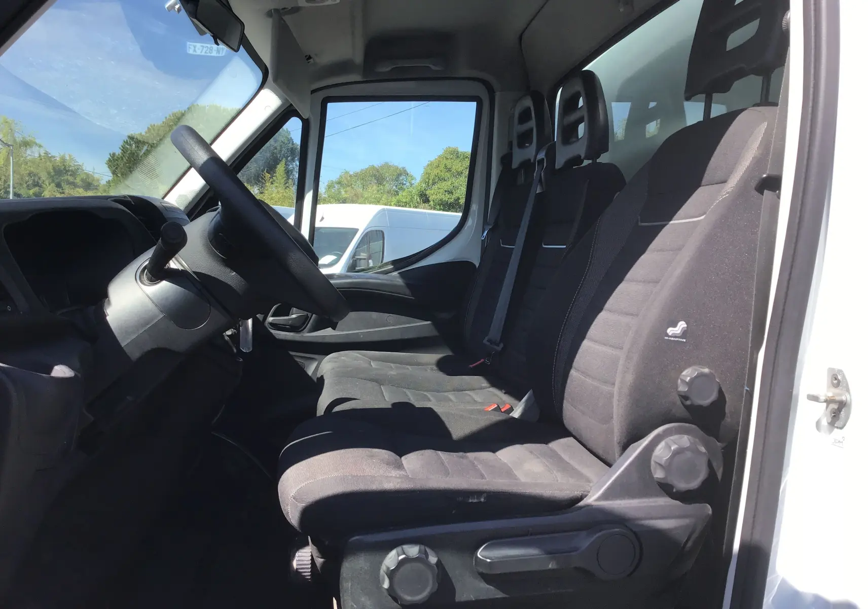 Vue intérieure côté conducteur de l'Iveco Daily Chassis Cabine blanc, montrant les sièges noirs et le volant.