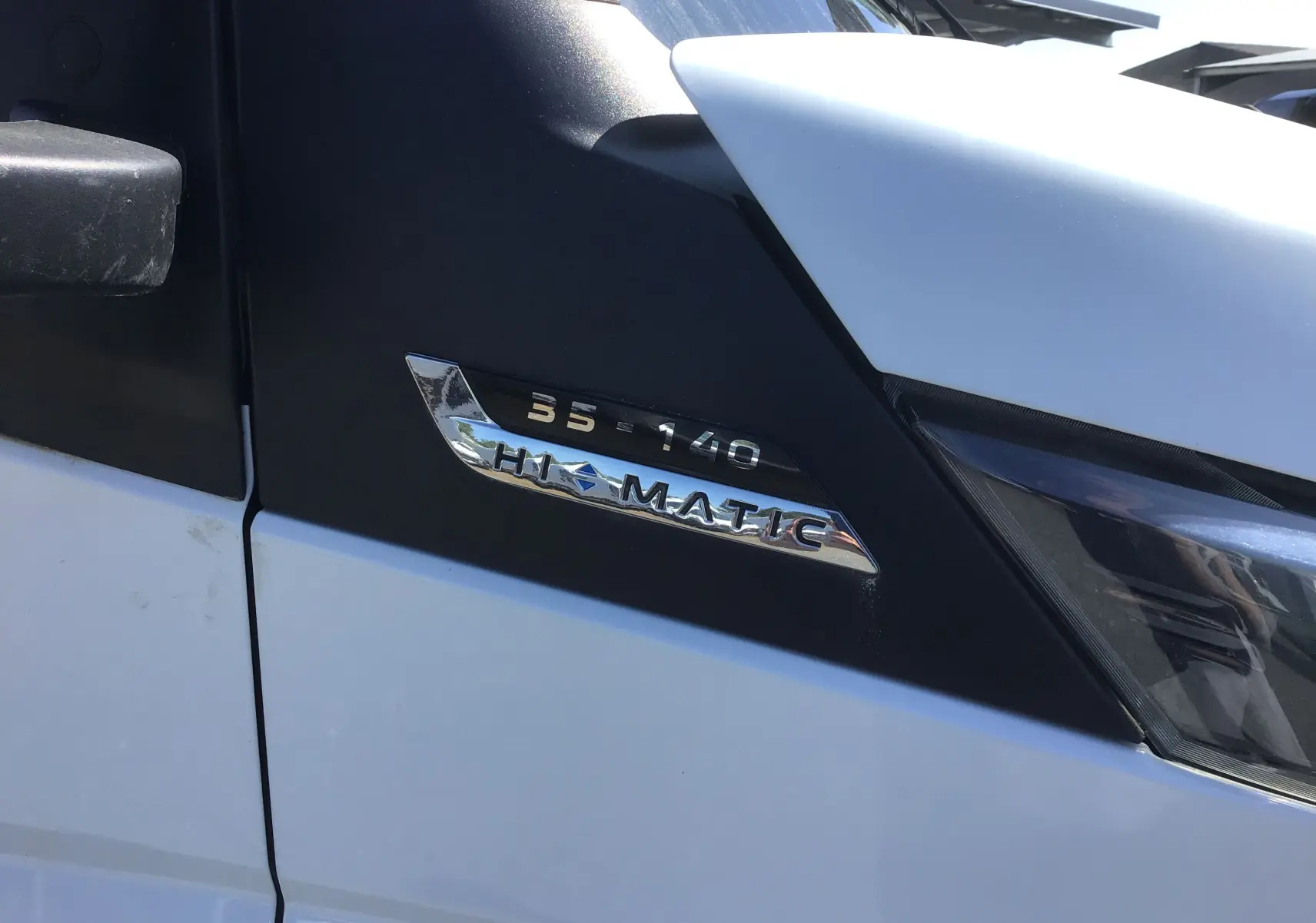 Gros plan sur l'insigne 35-140 HI-MATIC sur la porte côté gauche d'un Iveco Daily blanc.