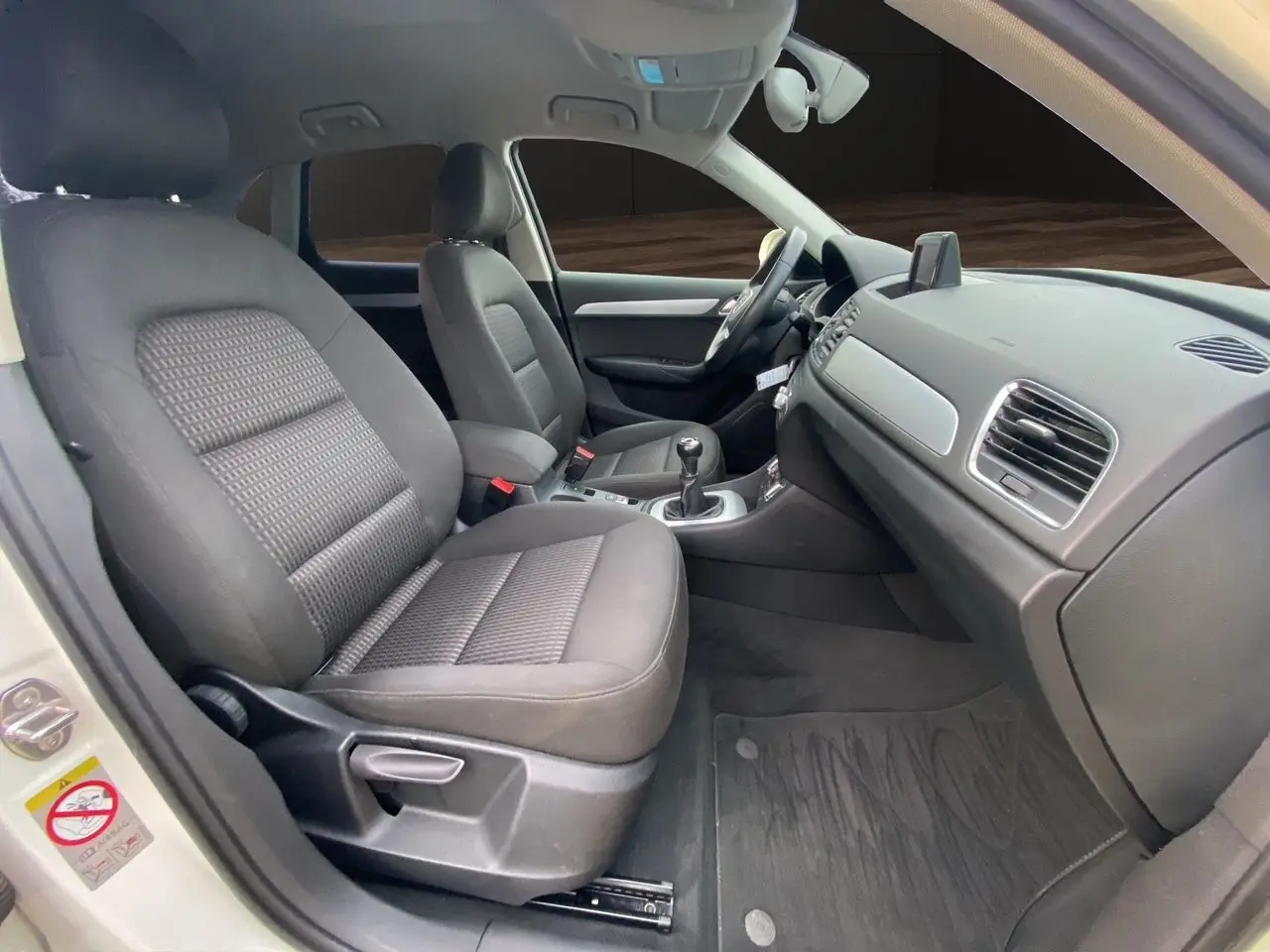 Vue intérieure côté conducteur de l'Audi Q3 blanc, montrant les sièges noirs en tissu et la console avec GPS intégré.