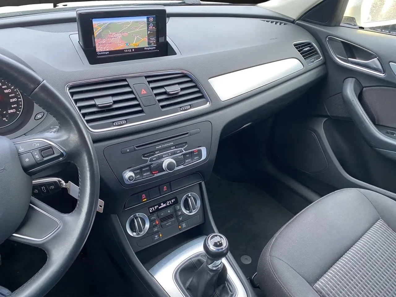 Vue intérieure côté passager avant de l'Audi Q3 2.0 TDI blanc, avec GPS intégré et boîte manuelle visible.
