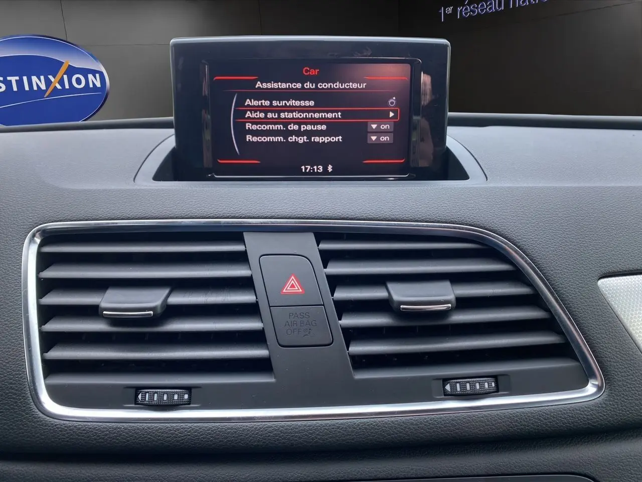 Vue intérieure du tableau de bord de l'Audi Q3 2014, écran central affichant l'aide au stationnement et les aérateurs noirs.