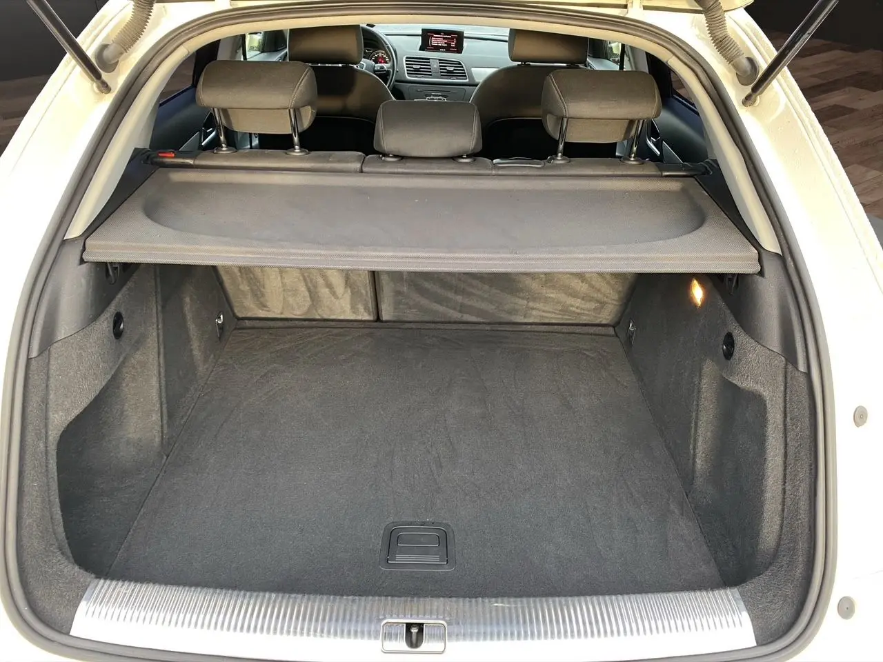 Coffre ouvert vu de l'arrière d'un Audi Q3 blanc 2014 avec cache-bagages et intérieur noir.