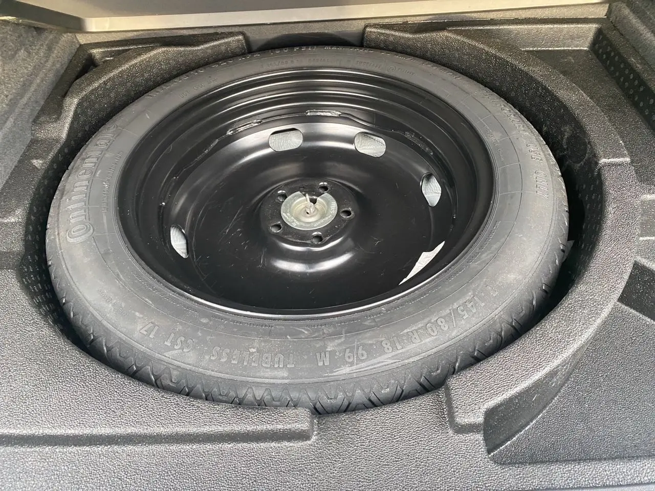 Roue de secours noire dans le coffre d’un Audi Q3 blanc, vue en plongée sur le pneu Continental.