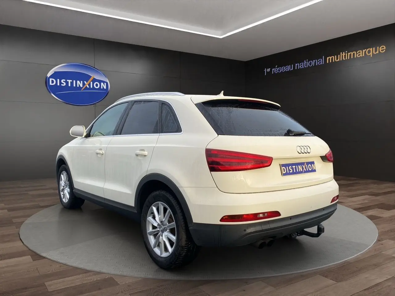 Audi Q3 blanc en 3/4 arrière droit, vitres arrière surteintées et attelage visibles dans un showroom.