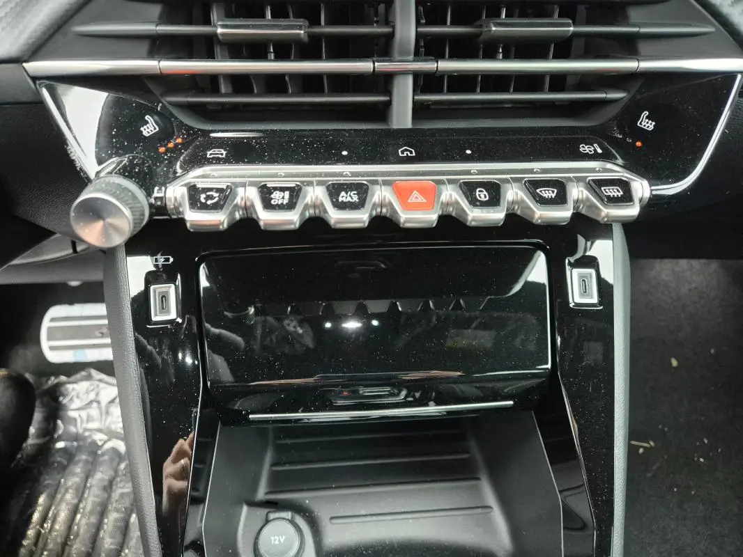 Gros plan sur la console centrale noire brillante du Peugeot 208 Hybrid 110 e-DCS6 GT avec boutons de commande et prise USB visibles.
