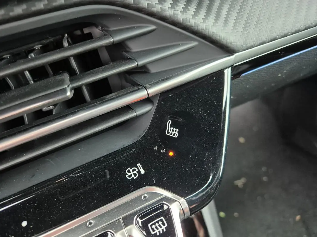 Détail du tableau de bord noir brillant de la Peugeot 208 gris, montrant le bouton de siège chauffant activé.