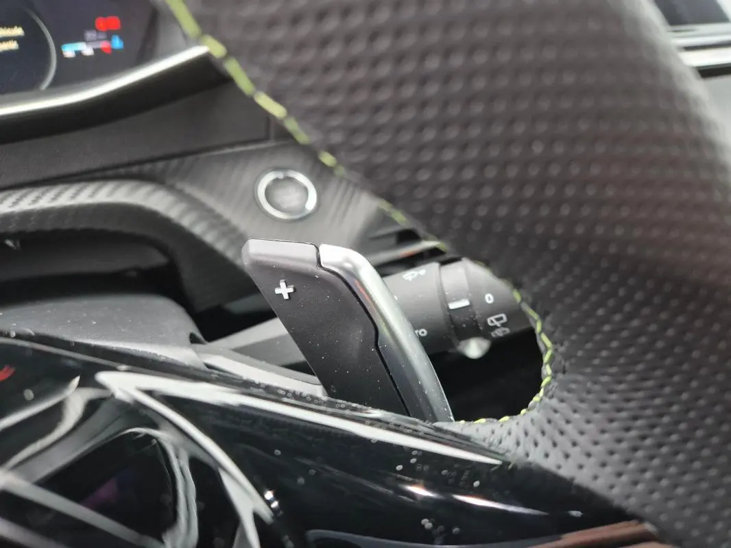 Gros plan sur la palette de changement de vitesse droite du volant perforé d’une Peugeot 208 Hybrid 110 e-DCS6 GT gris.