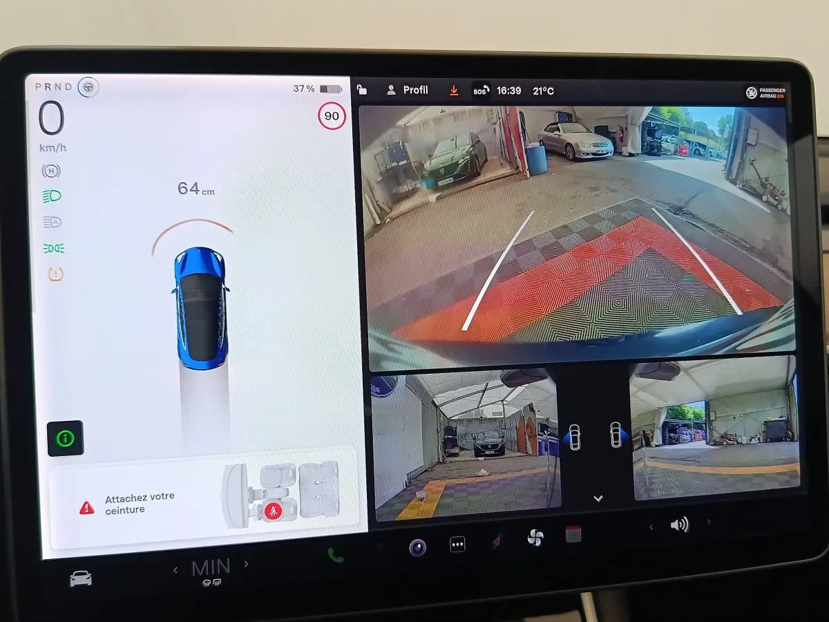 Écran tactile central montrant la caméra de recul et l'affichage du Tesla Model 3 bleu en stationnement.
