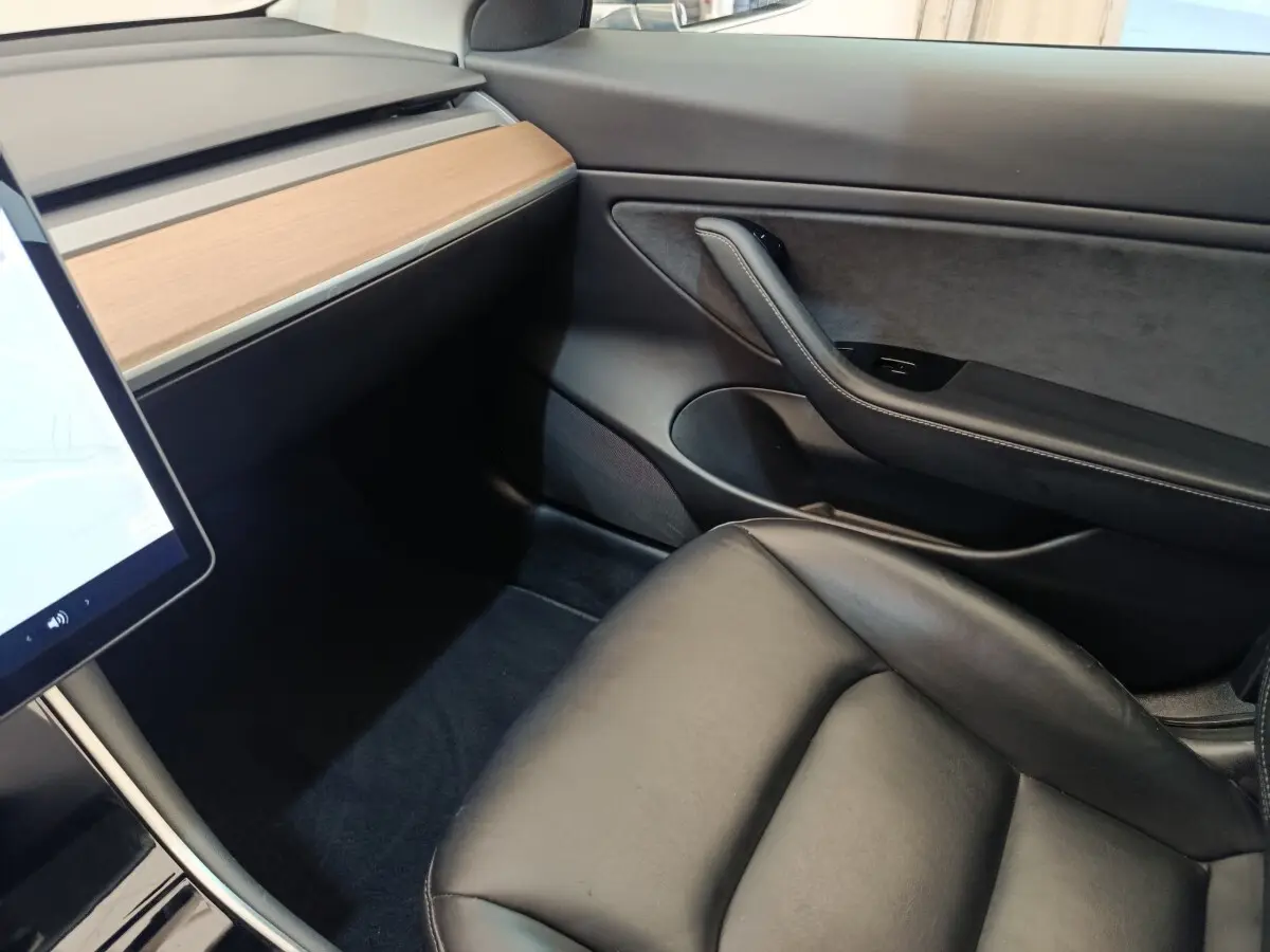 Vue intérieure côté passager d'une Tesla Model 3 2020 avec tableau de bord bois clair et siège cuir noir.