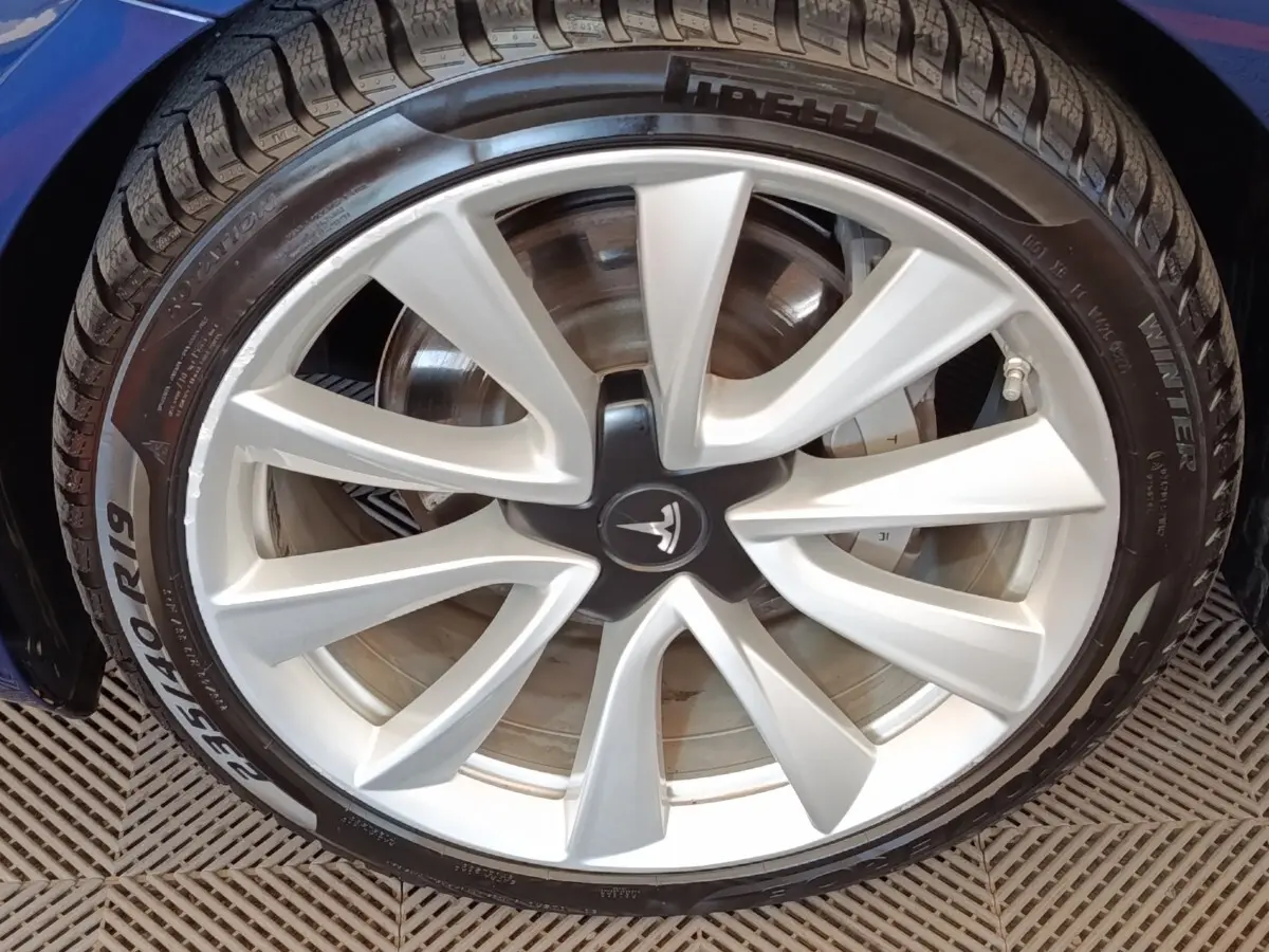 Gros plan sur la jante avant droite argentée d'une Tesla Model 3 Long Range bleu électrique.