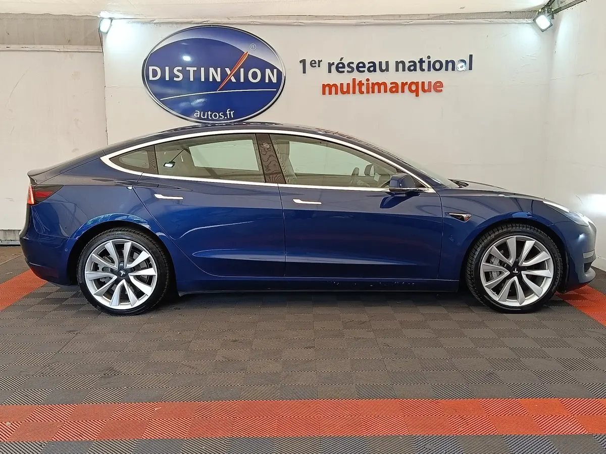 Profil latéral droit d'une Tesla Model 3 Long Range bleu électrique, avec jantes alliage et poignées affleurantes.