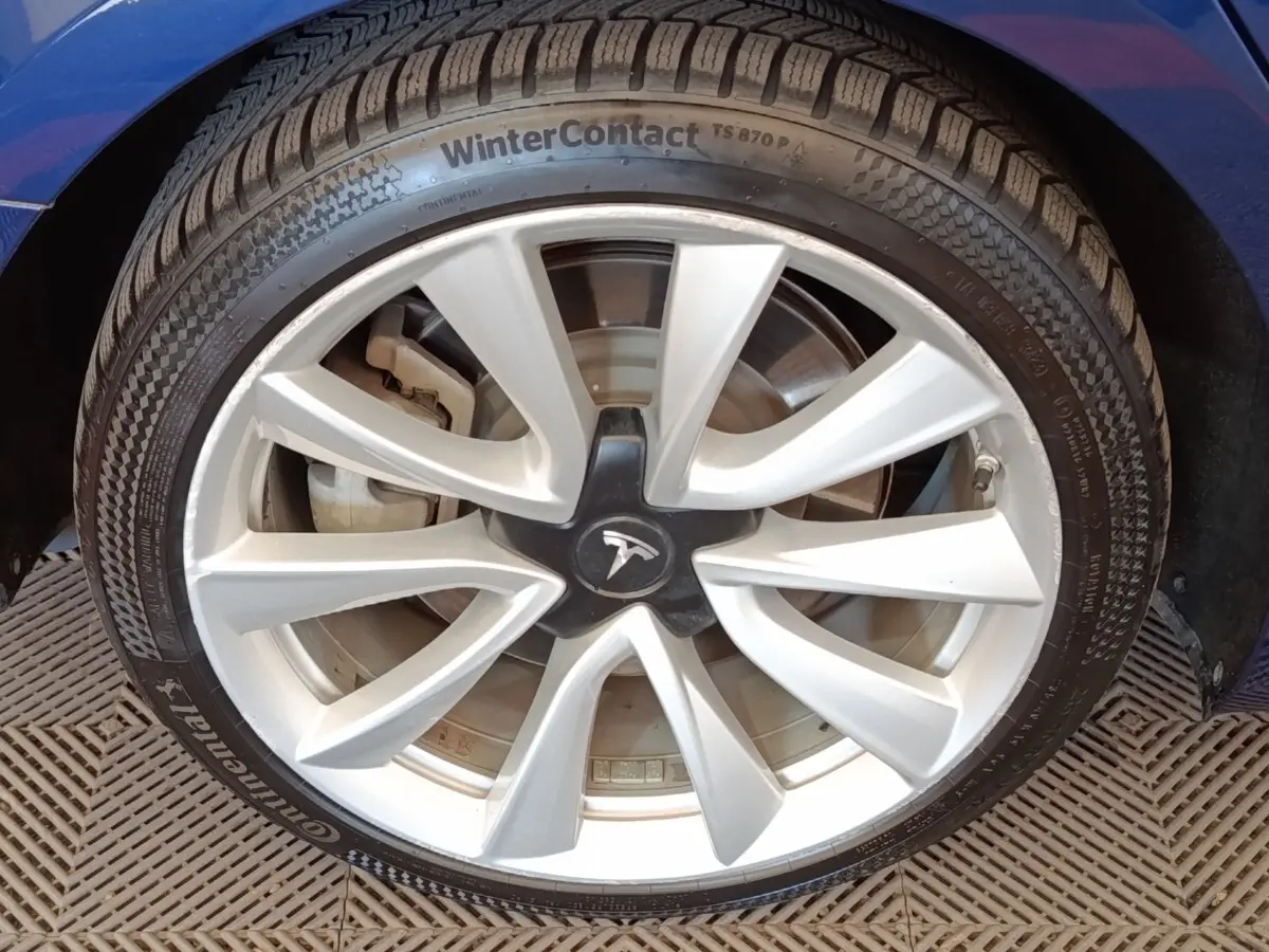 Gros plan sur la roue avant droite d’une Tesla Model 3 bleu, avec jante argentée et pneu hiver Continental.