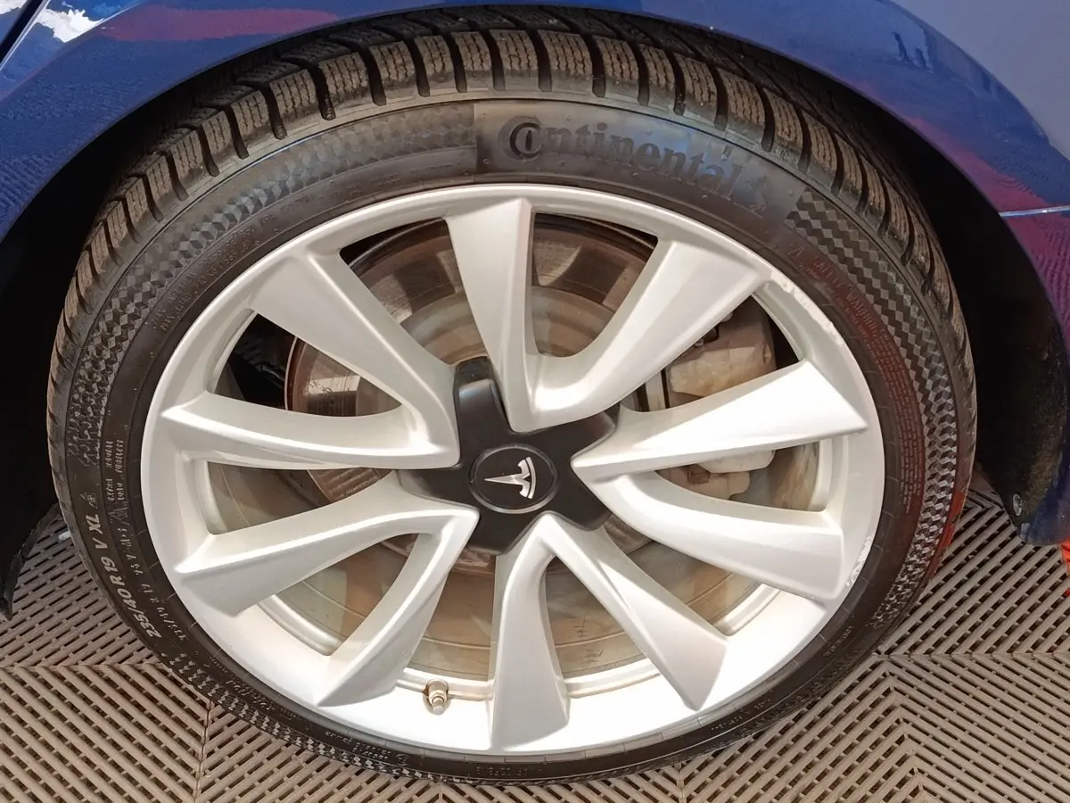Gros plan sur la roue avant gauche d’une Tesla Model 3 Long Range bleu avec jante argentée et logo Tesla au centre.