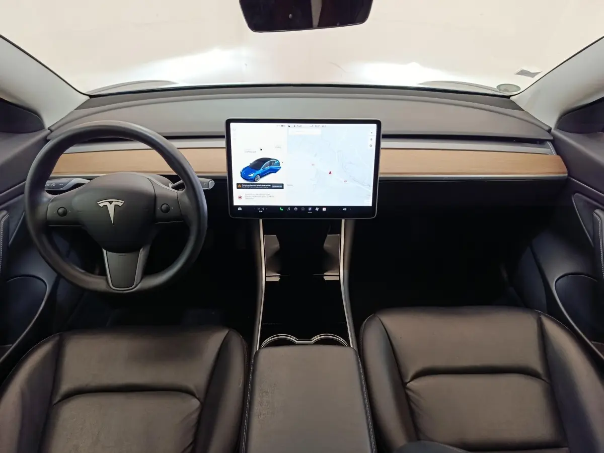 Vue intérieure frontale du tableau de bord et écran tactile central de la Tesla Model 3 Long Range bleu, sièges noirs en cuir.
