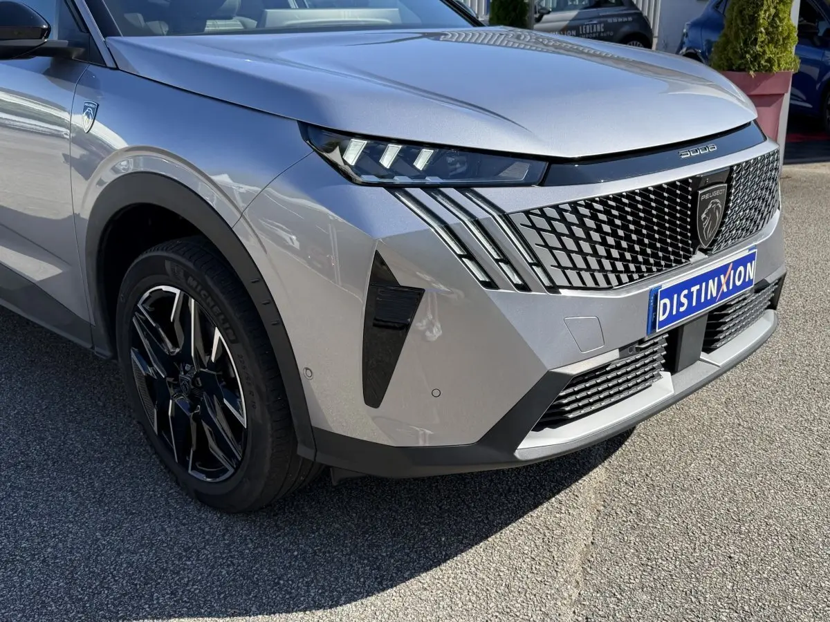 Peugeot 3008 gris clair en 3/4 avant droit, avec calandre distinctive et jantes noires brillantes.