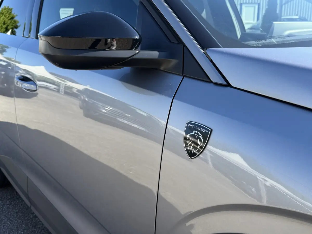 Gros plan sur le côté gauche gris clair du Peugeot 3008 2025 avec logo Peugeot et rétroviseur noir brillant.