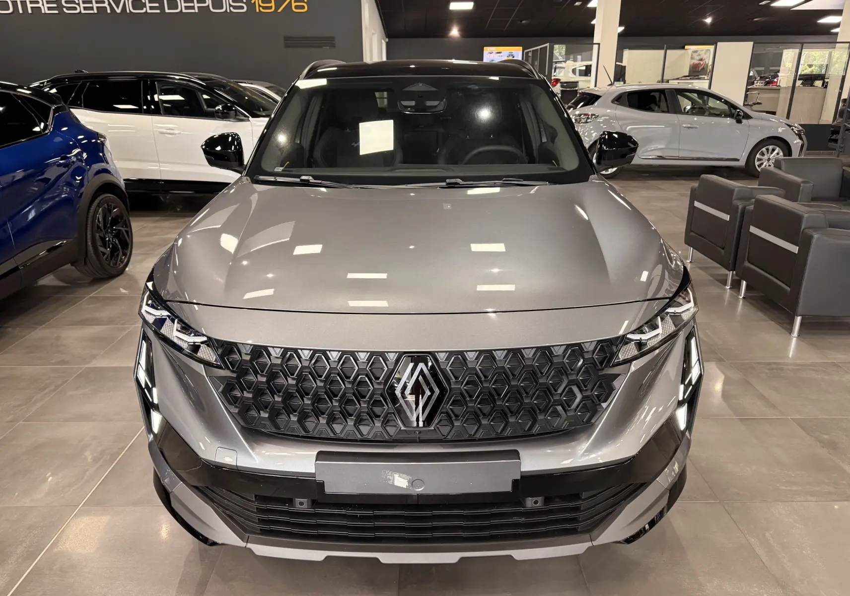 Vue avant d’un Renault Austral full hybrid gris schiste avec toit noir, calandre hexagonale et éclairage LED distinctif en showroom.