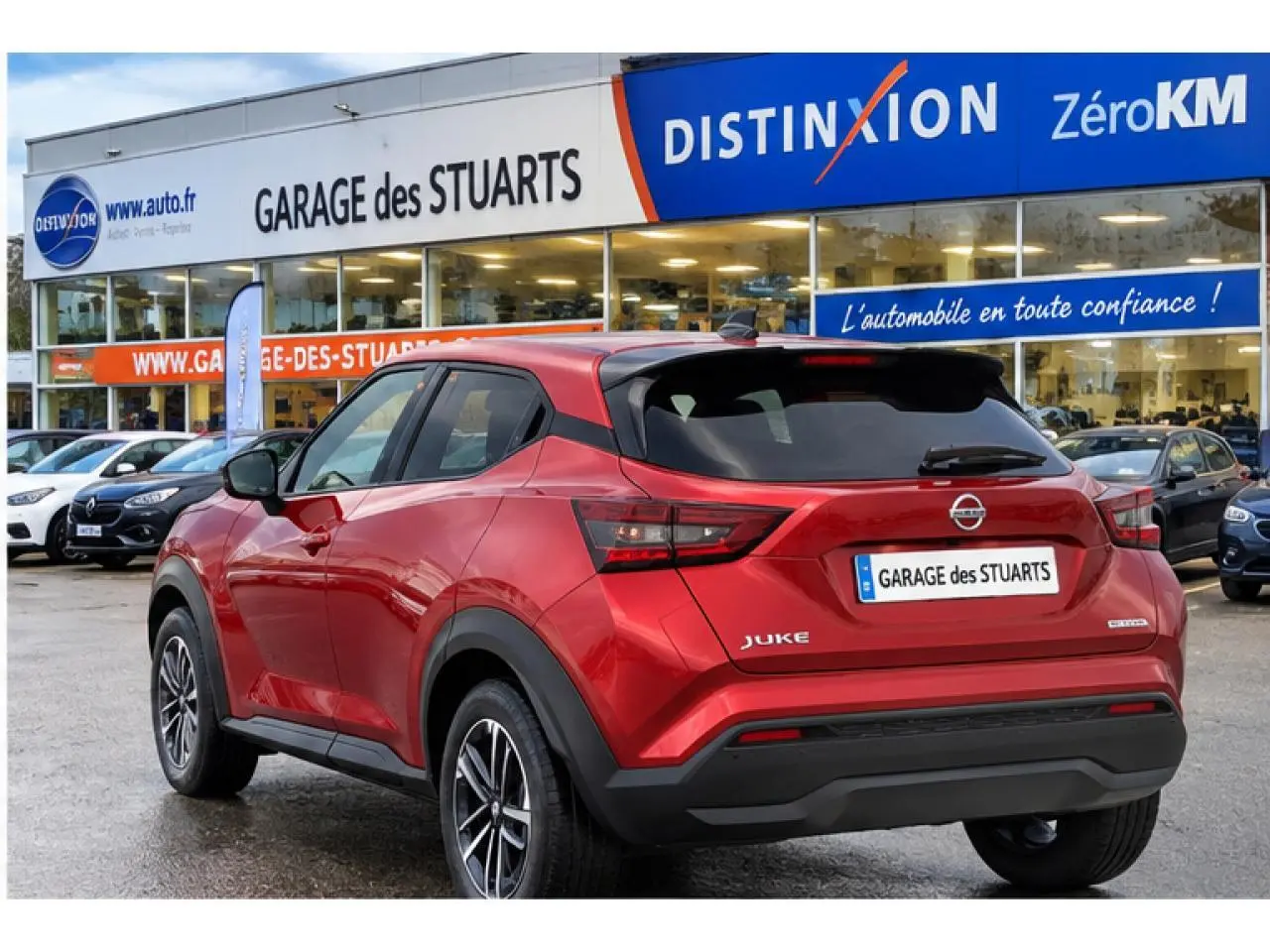 Vue 3/4 arrière droite du Nissan Juke rouge Fuji Sunset garé devant un garage avec jantes alliage 17 pouces.