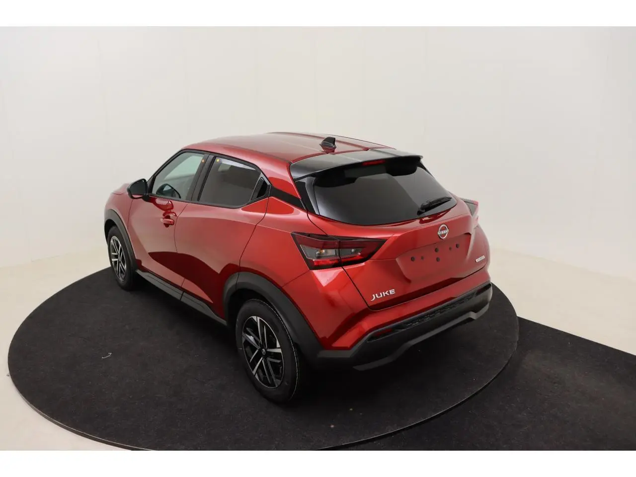 Vue 3/4 arrière droite du Nissan Juke 2026 rouge Fuji Sunset avec jantes alliage noires et vitres teintées.