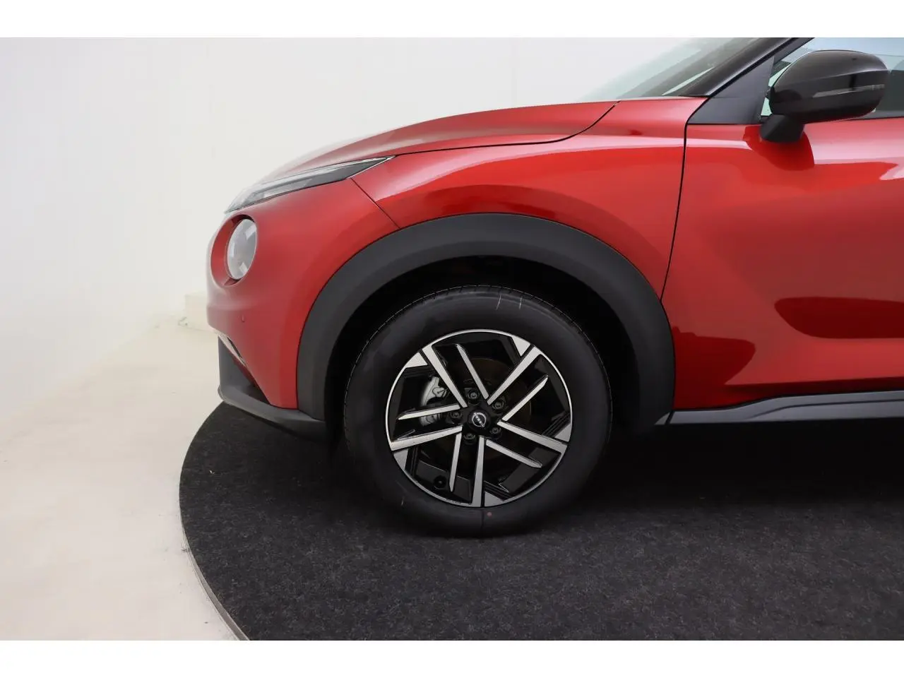 Gros plan sur la roue avant gauche et l'aile rouge Fuji Sunset du Nissan Juke 2026 avec jante alliage 17 pouces.