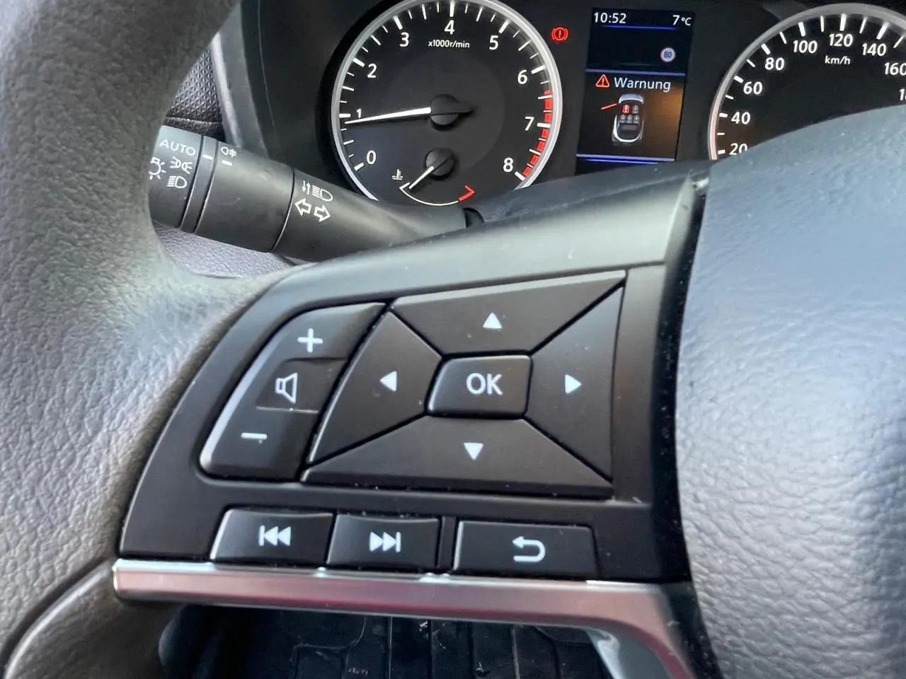 Gros plan sur les commandes au volant à gauche du Nissan Juke II gris Ceramic, avec compte-tours et écran digital en arrière-plan.