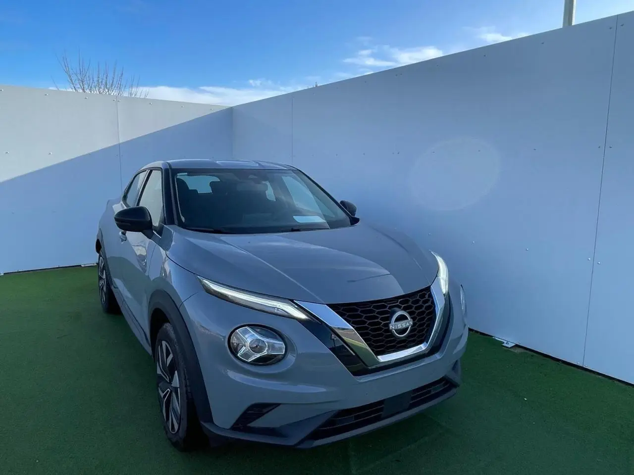 Nissan Juke II 2024 gris céramic en 3/4 avant droit, avec calandre chromée et jantes alliage noires.