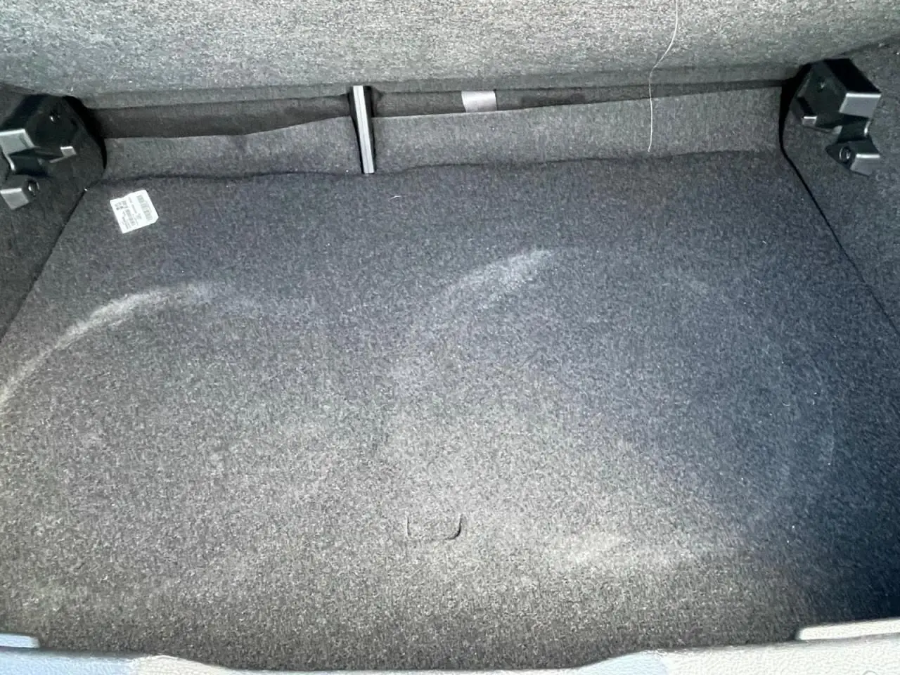 Vue rapprochée du coffre vide du Nissan Juke II 2024 en gris Ceramic, avec moquette grise et fixation arrière visible.