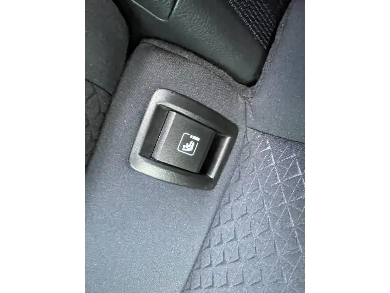 Gros plan sur le bouton de rabattement de siège arrière sur la banquette tissu gris du Nissan Juke II 2024.