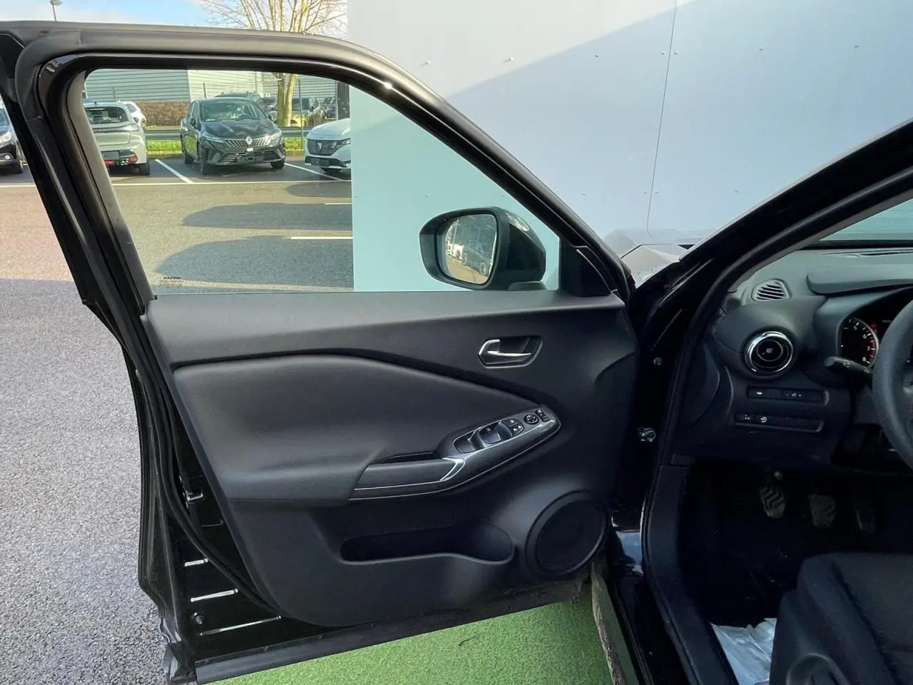 Intérieur côté conducteur du Nissan Juke II gris ceramic 2024, avec porte ouverte et commandes électriques visibles.