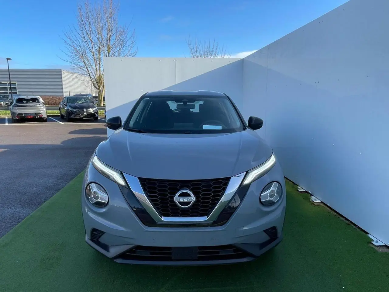 Nissan Juke II gris ceramic vu de face, soulignant sa calandre en V chromée et ses phares LED ronds.