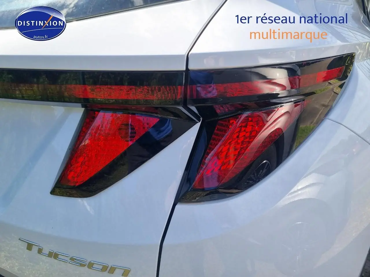 Gros plan sur le feu arrière droit rouge du Hyundai Tucson blanc atlas 2025 avec calandre grise et jante alliage visible en reflet.