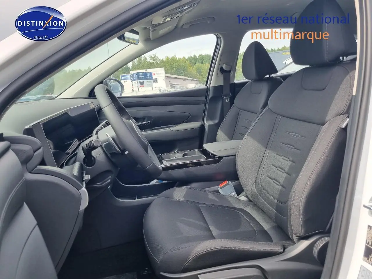Vue intérieure côté conducteur du Hyundai Tucson blanc atlas 2025 avec sièges tissu noirs et tableau de bord moderne.