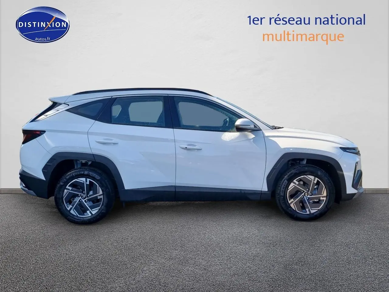 Profil droit d'un Hyundai Tucson blanc atlas 2025 avec jantes alliage et barres de toit noires visibles.