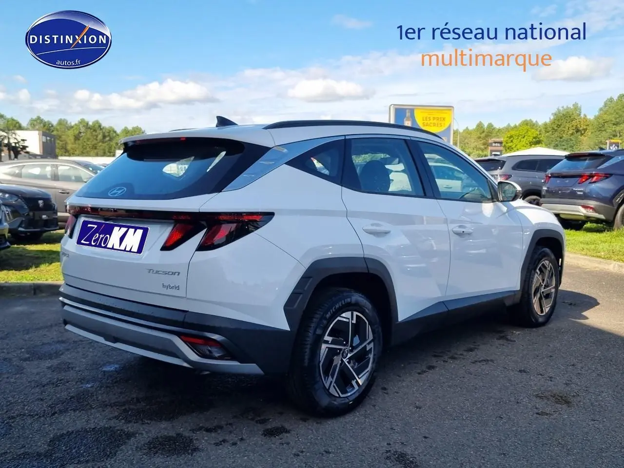 Vue 3/4 arrière droite du Hyundai Tucson blanc atlas hybride avec jantes alliage et barres de toit visibles.