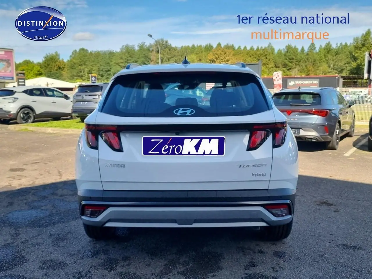 Vue arrière d'un Hyundai Tucson blanc atlas hybride avec feux arrière sombres et barres de toit visibles.