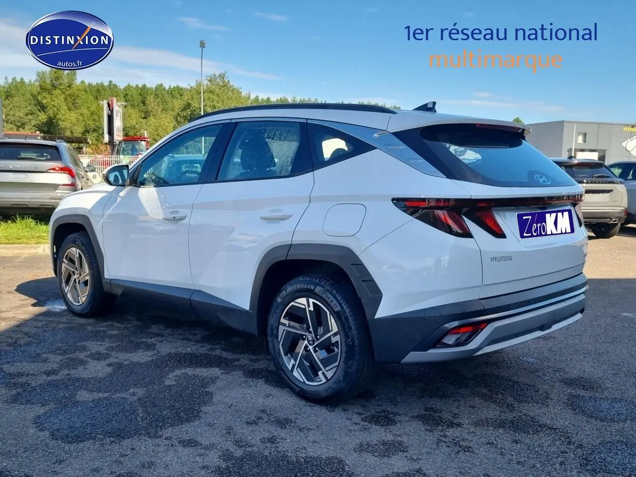 Vue 3/4 arrière droite du Hyundai Tucson blanc atlas avec jantes alliage et barres de toit noires sur parking extérieur.